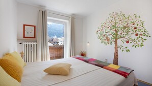 Una camera da letto con un letto, una finestra, un termosifone, un quadro appeso al muro e un murale con un albero.