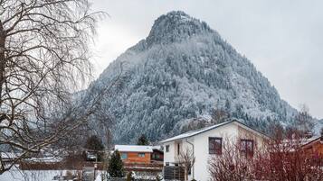 A mountain with a snow-covered peak, a white building with a red window, and a wooden fence in the foreground.