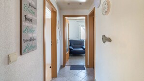 A hallway with a wooden door, a blue chair, a wall clock, and a key on the wall. - Apartment 'Am Hirnach' with Shared Terrace, Shared Garden and Wi-Fi (Sindelfingen)
