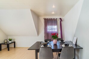 A dining area with a table set for four, a vase with flowers, and a window with curtains. - Apartment 'Am Hirnach' with Shared Terrace, Shared Garden and Wi-Fi (Sindelfingen)