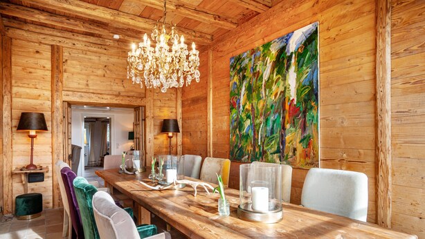 Un interior de madera con una mesa de comedor, sillas, una araña y un cuadro de colores.