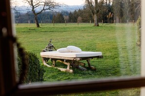 A rustic wooden bed with a mattress and pillows in a grassy field, viewed through a window with a metal frame. - Chalet "Windhäusern 5" with Mountain View, Shared Garden & Wi-Fi (Wangen im Allgäu)