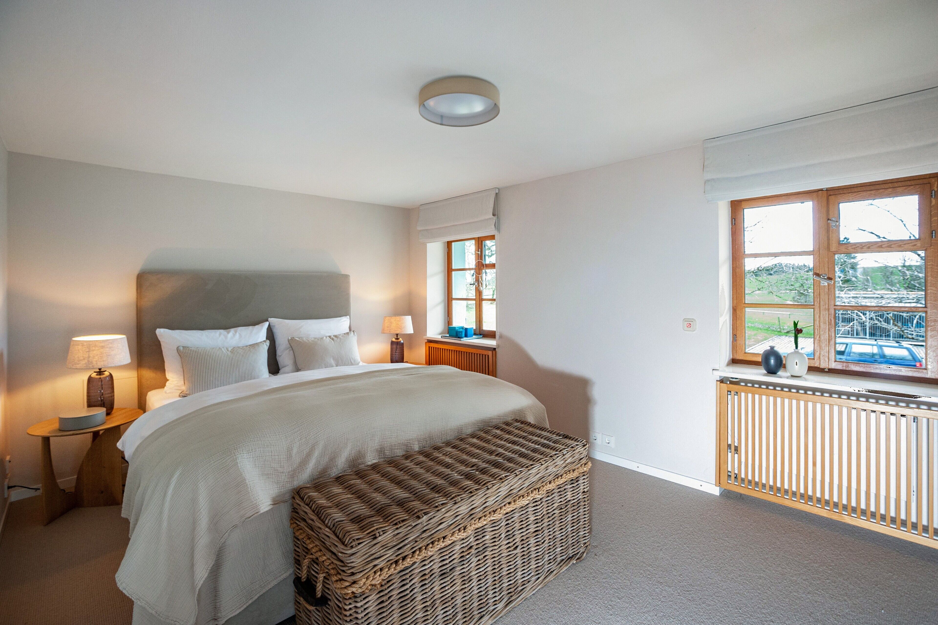 A bedroom with a bed, bedside lamps, a window, and a view of the outdoors.