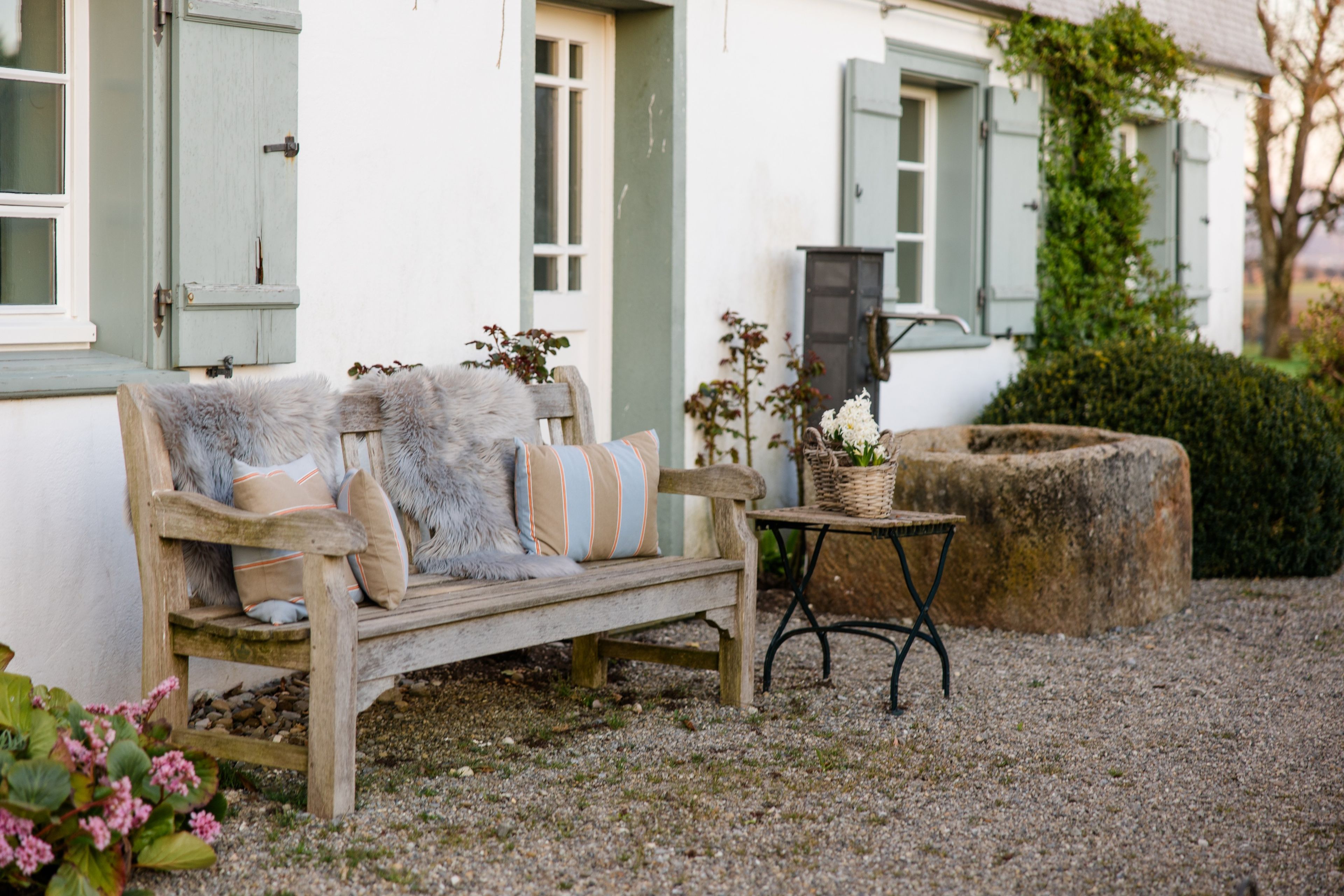 Un espace extérieur rustique aménagé avec un banc en bois et une petite table, entouré de gravier et de verdure.