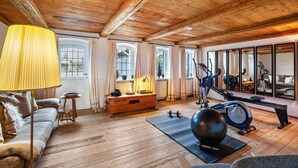 Una habitación con suelo de madera, un sofá, una lámpara, equipo de ejercicio y ventanas amplias.
