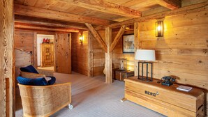 Interior de una cabaña de madera con una silla de mimbre, un cofre de almacenamiento Berg y una lámpara fijada a la pared.