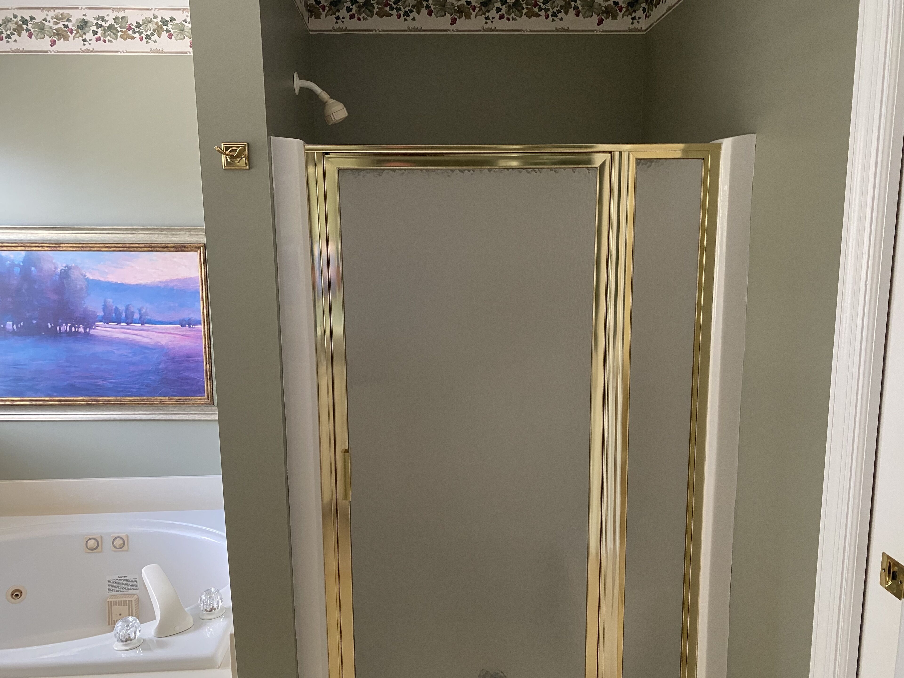 A bathroom with a bathtub, a shower with gold trim, and a floral wallpaper border.