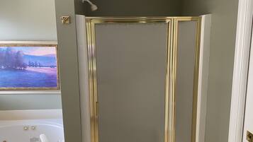 A bathroom with a bathtub, a shower with gold trim, and a floral wallpaper border.