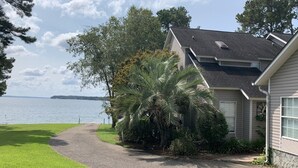 A house with a gravel driveway leading to a grassy area, a palm tree, and a view of a lake. - Beautiful 2BR/2.5 BA - Lakefront, Private Dock & Boat Ramp. Starlink Internet. (Abbeville)