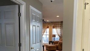 A hallway leading to a living room with a ceiling fan, a door with a security camera, and a window with curtains. - Beautiful 2BR/2.5 BA - Lakefront, Private Dock & Boat Ramp. Starlink Internet. (Abbeville)