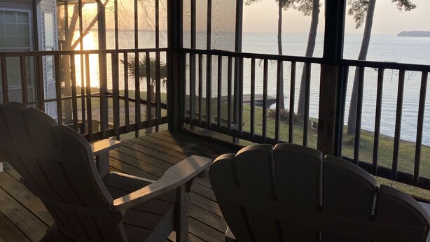 A covered deck with wooden chairs, overlooking a body of water and trees. - Beautiful 2BR/2.5 BA - Lakefront, Private Dock & Boat Ramp. Starlink Internet. (Abbeville)