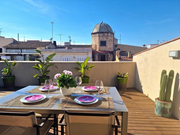 Une terrasse sur le toit, avec une table dressée pour le dîner, entourée de plantes en pot et d’un cactus.