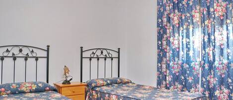 Quarto com duas camas, mesa de cabeceira, abajur e cortinas florais.