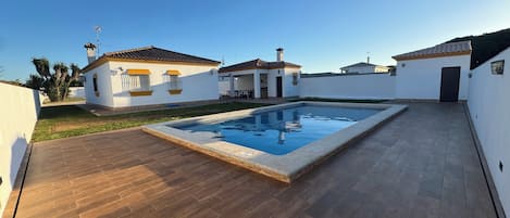 Propiedad residencial con piscina, terraza de madera y paredes blancas.