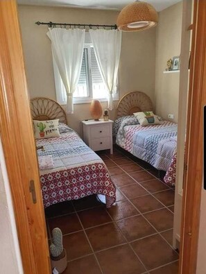 Quarto com duas camas, uma mesa de cabeceira, janela com cortinas e luminária suspensa.