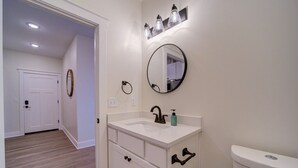 A bathroom with a white vanity, a round mirror, and a toilet. - Stay on Clay - Suite #6 (Muskegon)