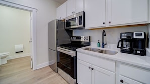 A compact kitchen with white cabinets, a stainless steel refrigerator, a microwave, a stove, and a coffee maker. - Stay on Clay - Suite #6 (Muskegon)