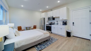 Une chambre d’hôtel de taille réduite, comprenant un lit, une petite kitchenette, une table à manger et une poubelle.