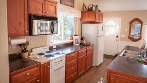 A kitchen with wooden cabinets, a stove, a refrigerator, and a window with a view of trees. - A beautiful Retreat on beautiful Hayden Lake nestled among the gorgeous pines (Hayden)
