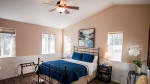 A bedroom with a bed, a ceiling fan, a window, a nightstand, a lamp, and a painting on the wall. - A beautiful Retreat on beautiful Hayden Lake nestled among the gorgeous pines (Hayden)