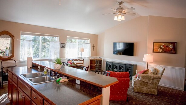 A spacious kitchen with a large island, a dining area with a red sofa, and a television mounted on the wall. - A beautiful Retreat on beautiful Hayden Lake nestled among the gorgeous pines (Hayden)