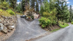 A house with a driveway leading to a garage, surrounded by trees and a stone wall. - A beautiful Retreat on beautiful Hayden Lake nestled among the gorgeous pines (Hayden)