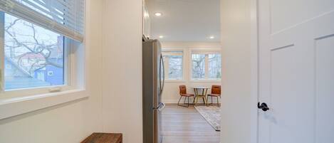 A hallway with a bench, a refrigerator, and a dining area with chairs and a table.