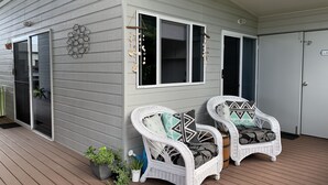 A porch with two white wicker chairs with patterned cushions, a small potted plant, and a decorative wall piece. - Peaceful Oasis at Cooloola Cove (Cooloola Cove)