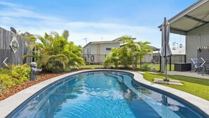 A swimming pool with a curved edge, surrounded by a wooden fence and palm trees. - Peaceful Oasis at Cooloola Cove (Cooloola Cove)