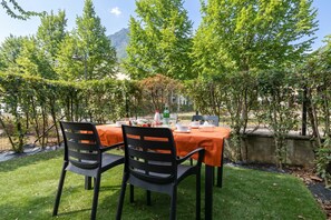 An outdoor dining area with a table set for two, surrounded by greenery and a mountain in the background. - Porto Letizia Paganini 3, Porlezza, Italy (Porlezza)