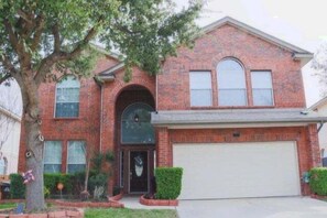 A two-story brick house with a garage, a front door, and a large tree in the front yard.