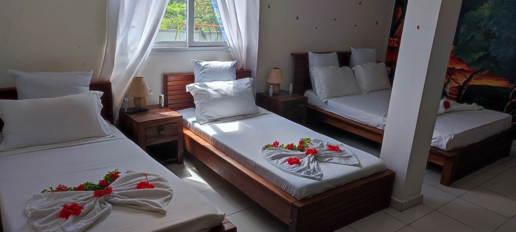 A hotel room with two single beds, a double bed, and a small table with a lamp.