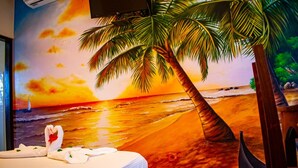 Un dormitorio con un mural de una playa al atardecer, una cama con ropa de cama blanca y un cabecero de madera.