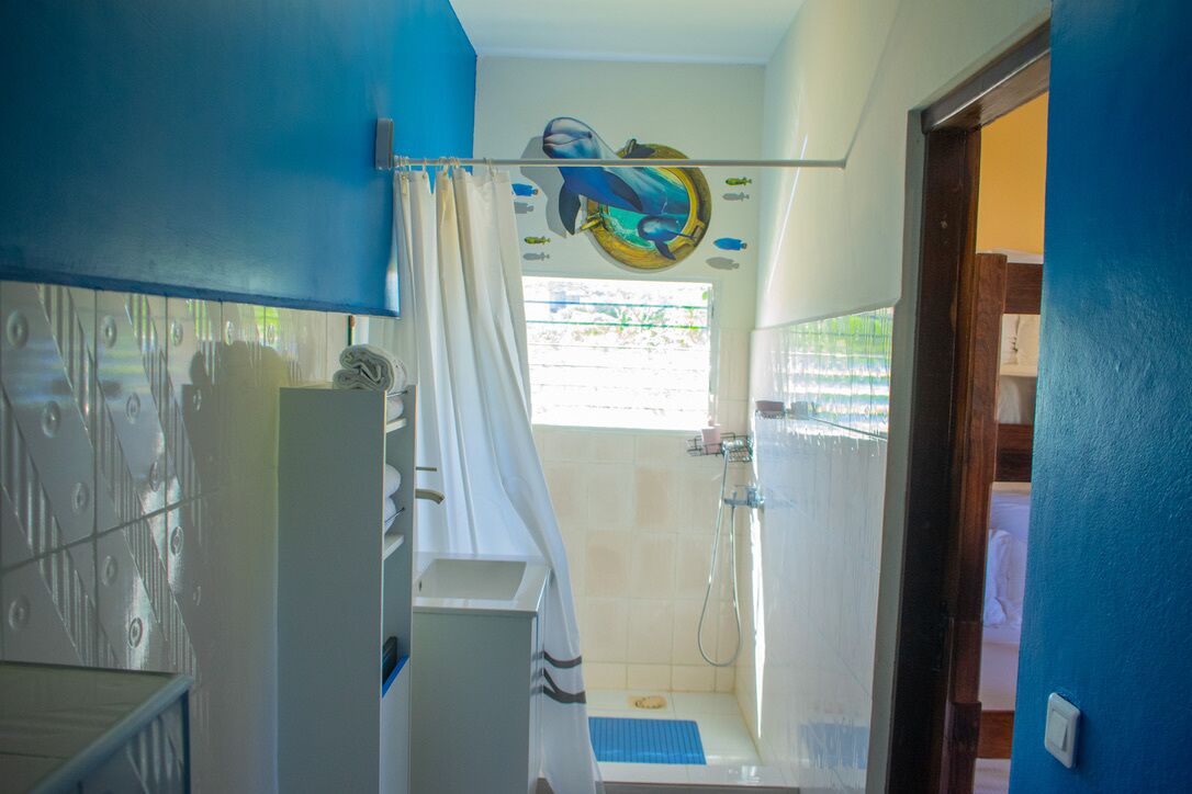A bathroom with a shower, a toilet, and a sink. There is a curtain and a wall decal of a whale.