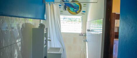 A bathroom with a shower, a toilet, and a sink. There is a curtain and a wall decal of a whale.