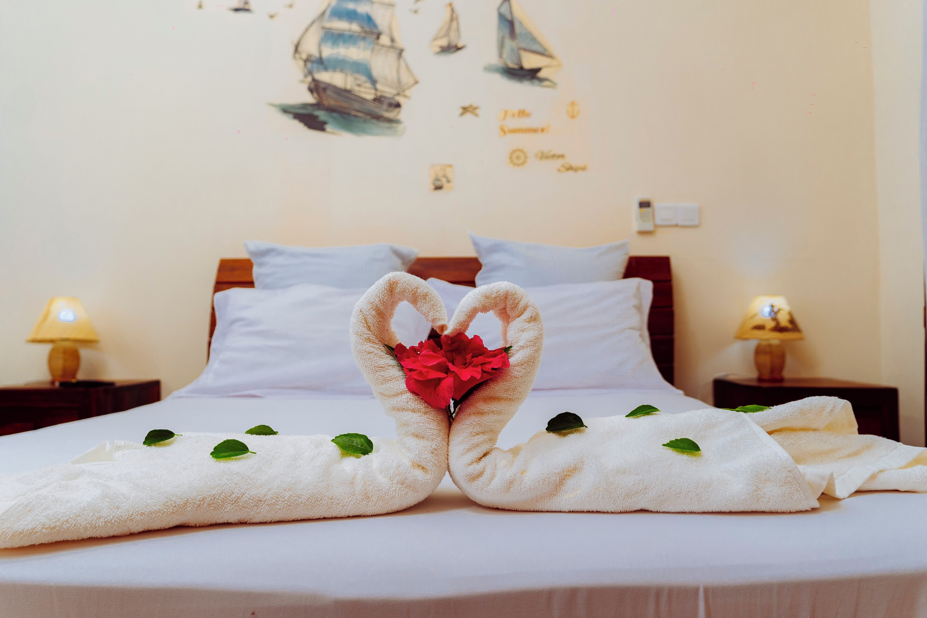 Una cama con toallas dispuestas en forma de corazón, una flor roja y hojas verdes sobre la cama.