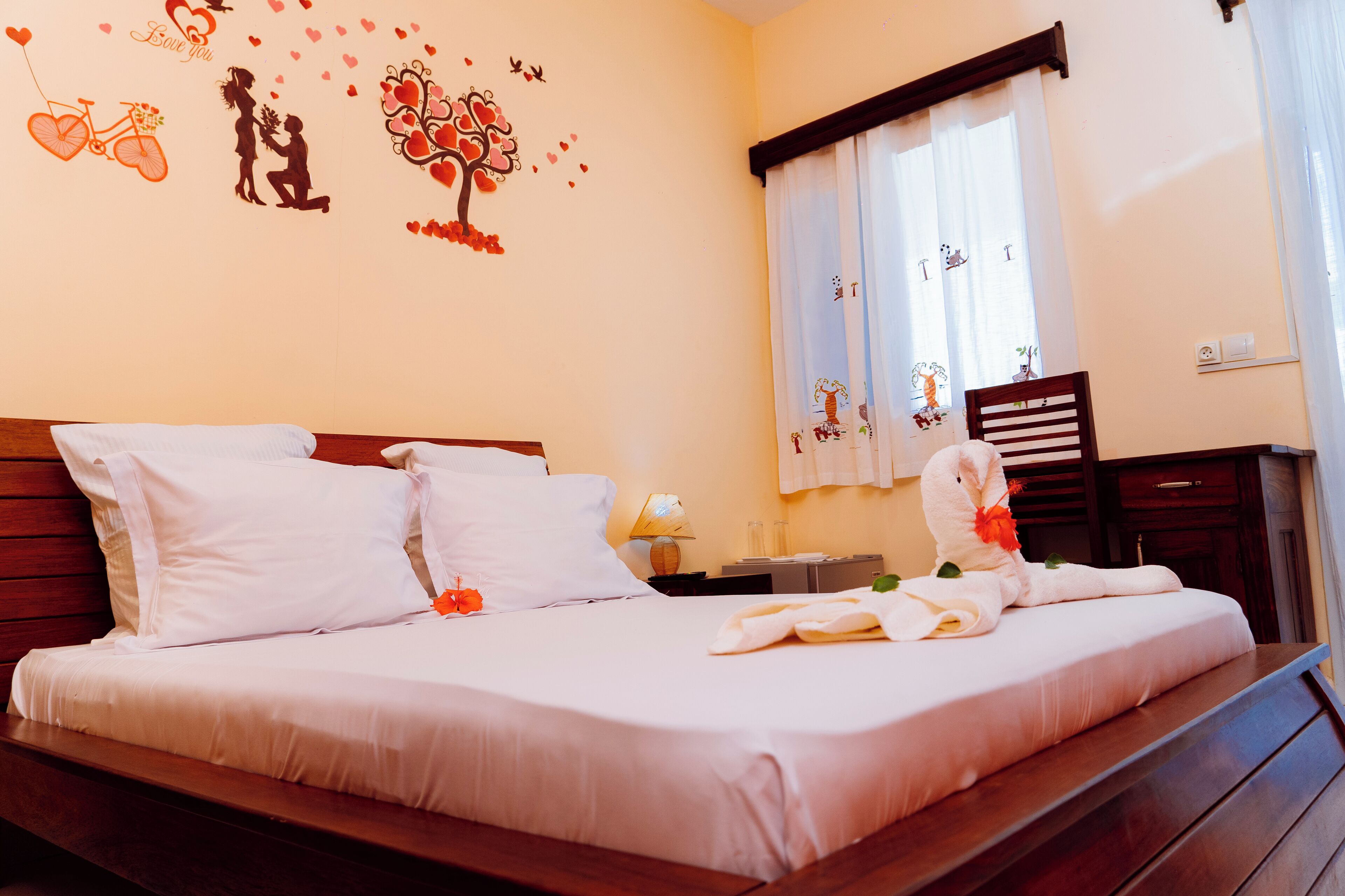 A neatly made bed with white linens, a wooden headboard, and a decorative wall with heart motifs and a bicycle.