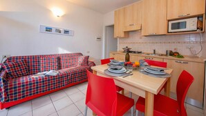 A compact living space with a sofa, dining table, chairs, and a kitchenette. - Porto Letizia Roma 1, Porlezza, Italy (Porlezza)