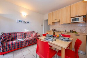 Ein kompakter Wohnbereich mit einer Couch, Esstisch, Stühlen, einer Mikrowelle und einer gefliesten Spritzschutzwand.