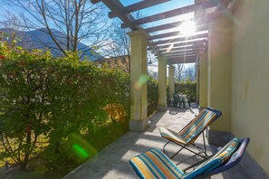Eine überdachte Terrasse mit zwei gestreiften Liegestühlen, einer Pergola und Blick auf die Berge.