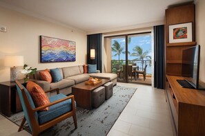 Relax in a spacious living area with a sofa set, flat-screen TV, and sliding glass door leading to a balcony with ocean views.