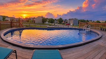 Una piscina con plataforma de madera, rodeada por un barrio residencial al atardecer.