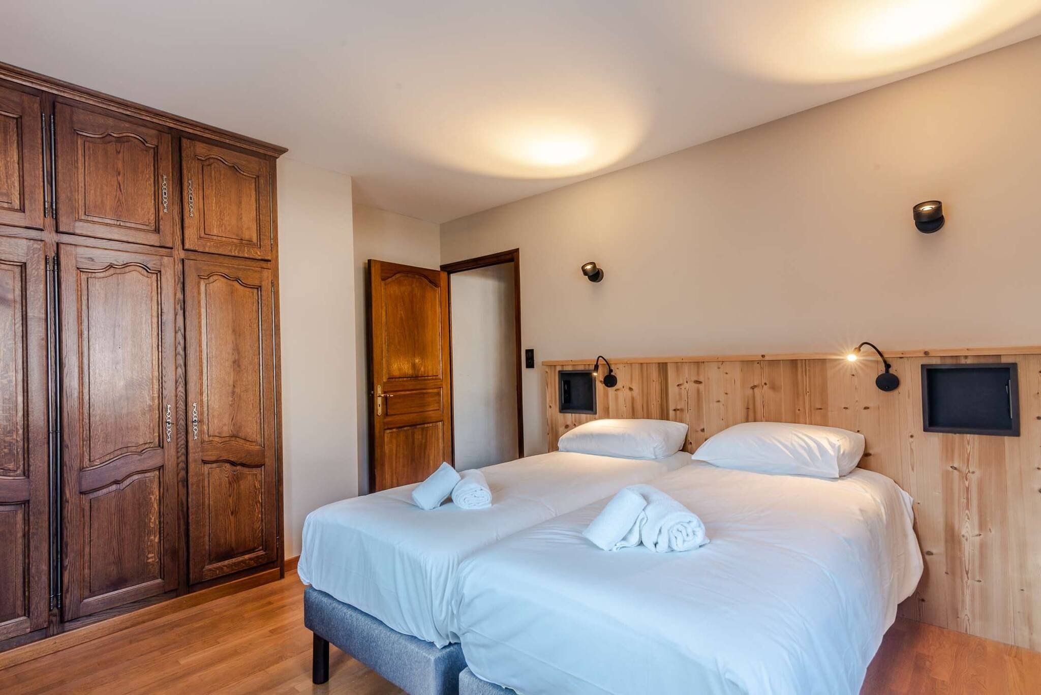 A hotel room with a large wardrobe, a bed with white linens, and two wall-mounted light fixtures.
