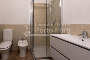 A bathroom with a toilet, bidet, glass-enclosed shower, and a sink.