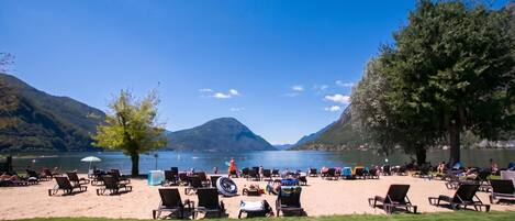 Une plage au bord d’un lac, avec des chaises longues et des tables, entourée de montagnes et offrant une vue sur un ciel dégagé.