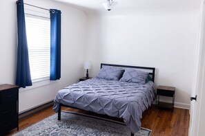 A bedroom with a bed, a nightstand, a dresser, and a window with curtains.