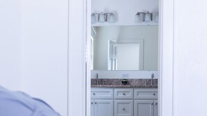 Een slaapkamer met een bed, een badkamer met een wastafel en kastjes, en een spiegel.