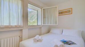 A hotel room with a bed, two windows, a radiator, and a framed picture on the wall. - Porto Letizia Ortensia 8, Porlezza, Italy (Porlezza)