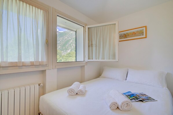 A hotel room with a bed, two windows, a radiator, and a framed picture on the wall.