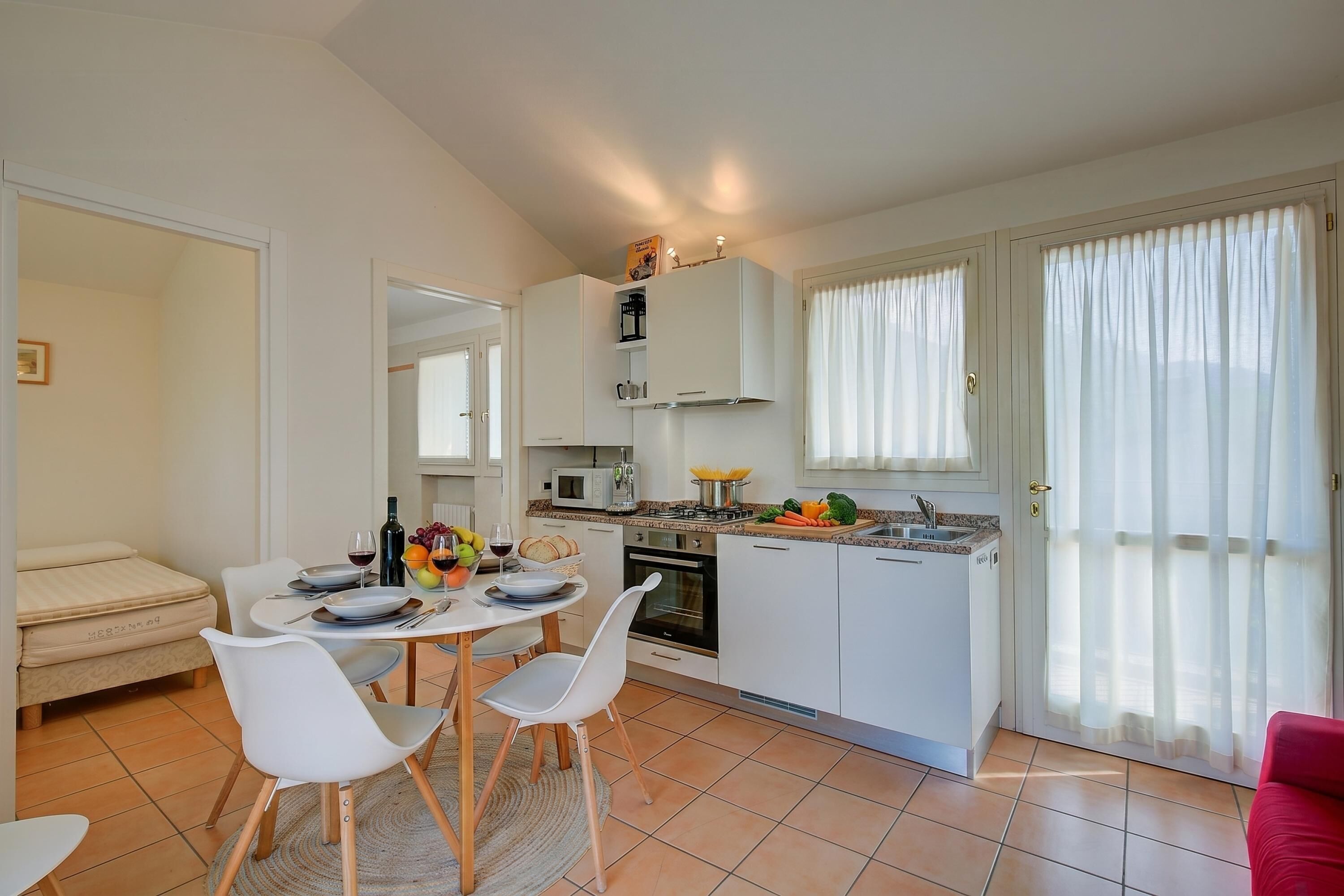 A compact kitchen with white cabinets, a dining table with chairs, a microwave, and a stove.